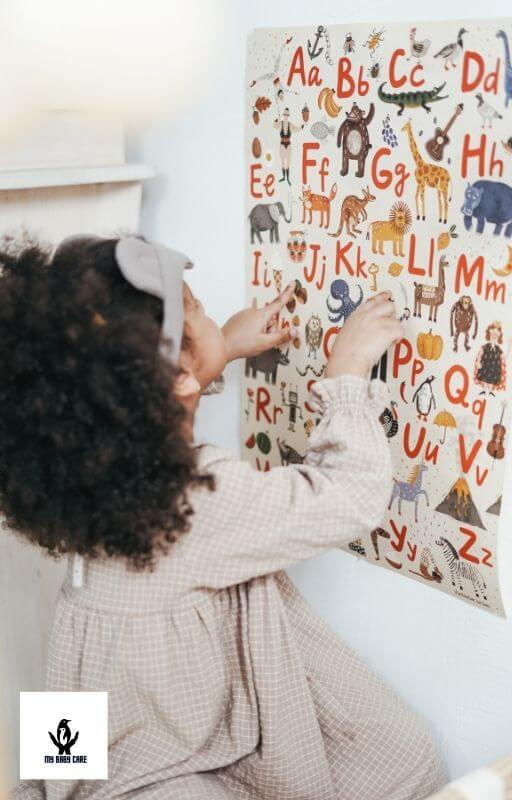 beautiful baby girl points to letters on a wall poster
